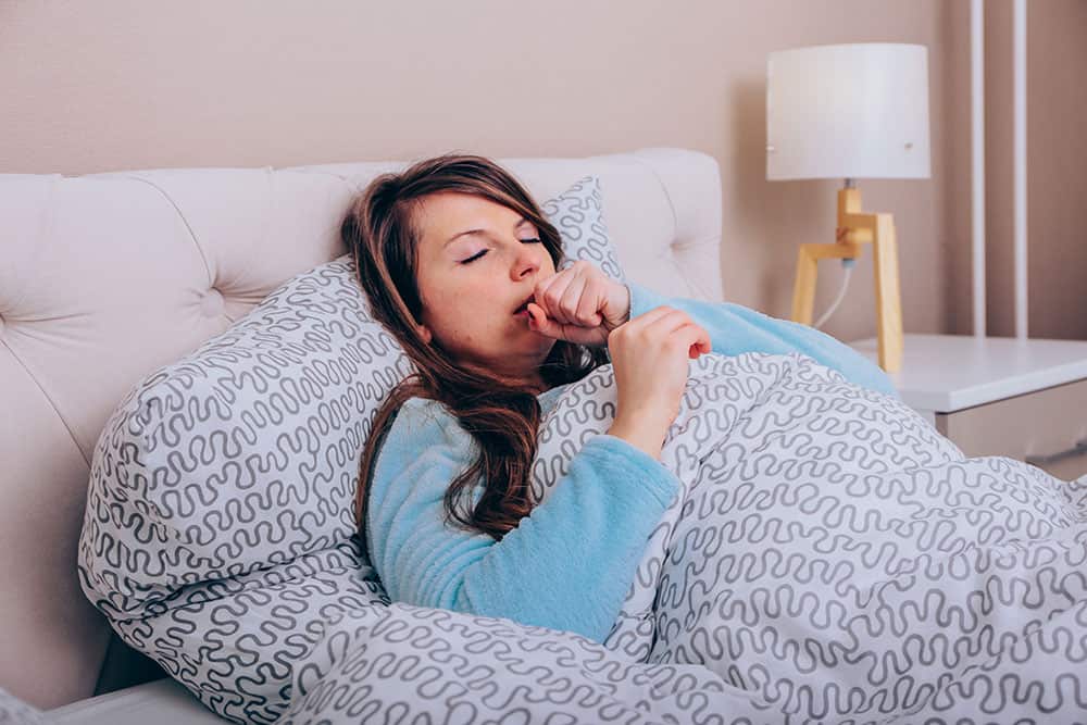 Junge Frau liegt hustend im Bett