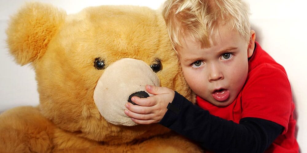 Kleiner Junge hustet und kuschelt mit Teddybär