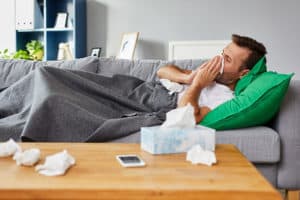 Mann liegt mit einer Decke auf der Couch und putzt sich die Nase
