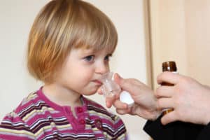 Kleines Mädchen bekommt einen Becher mit Hustensaft