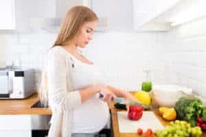 Schwangere Frau schneidet eine Paprika in der Küche