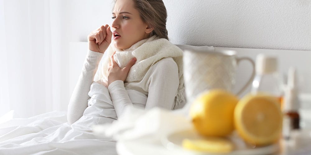 Junge Frau sitzt im Bett im Husten Im Vordergrund Zitronen und Hustensaft