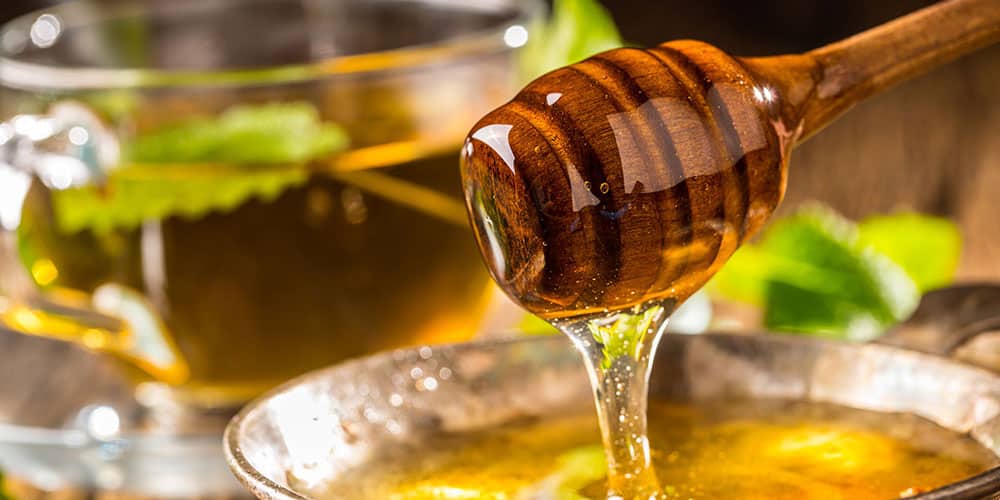 Honig wird mit einem Stab in ein Glas Tee gegeben