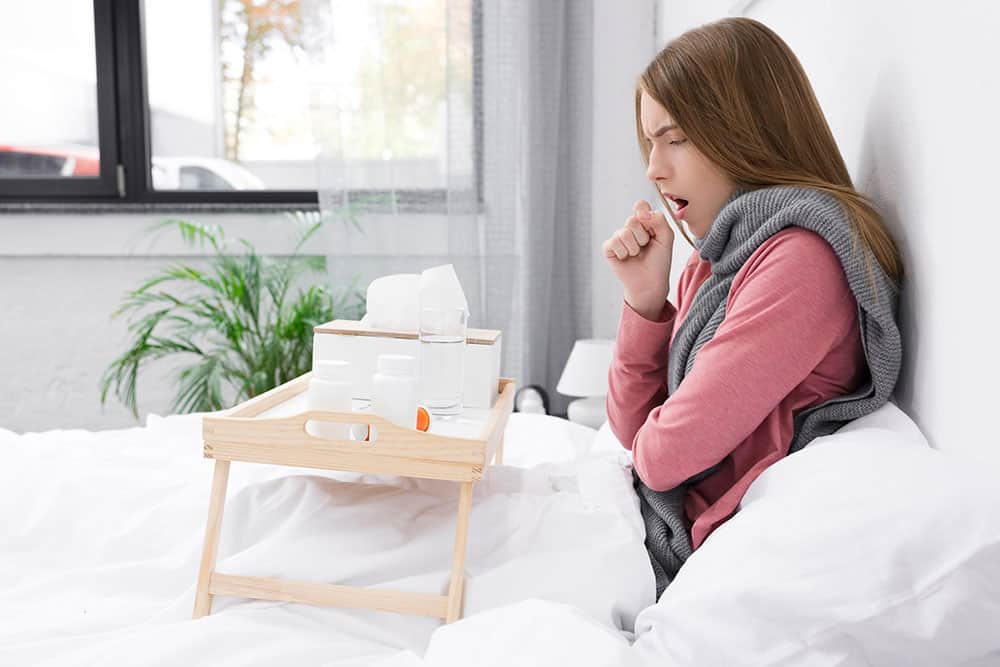 Junge Frau mit akuter Bronchitis sitzt im Bett
