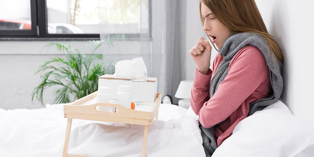 Junge Frau mit Bronchitis sitzt im Bett